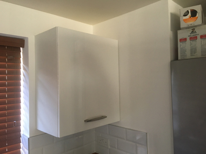 a white gloss kitchen wall cabinet fitted on a wall in a timber framed house